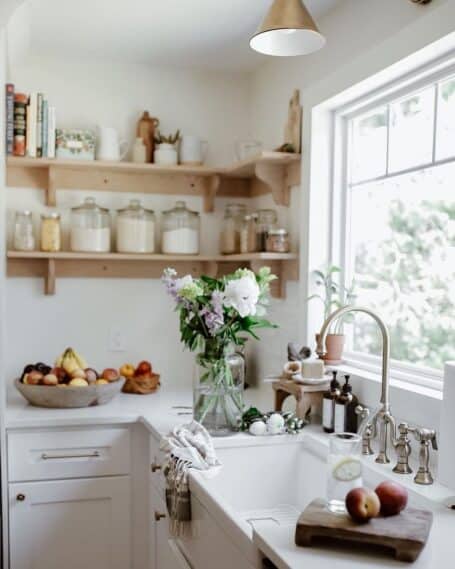 beautiful-kitchen-sink-by-window-open-shelves-glass-jars-brass-sconce-455x569